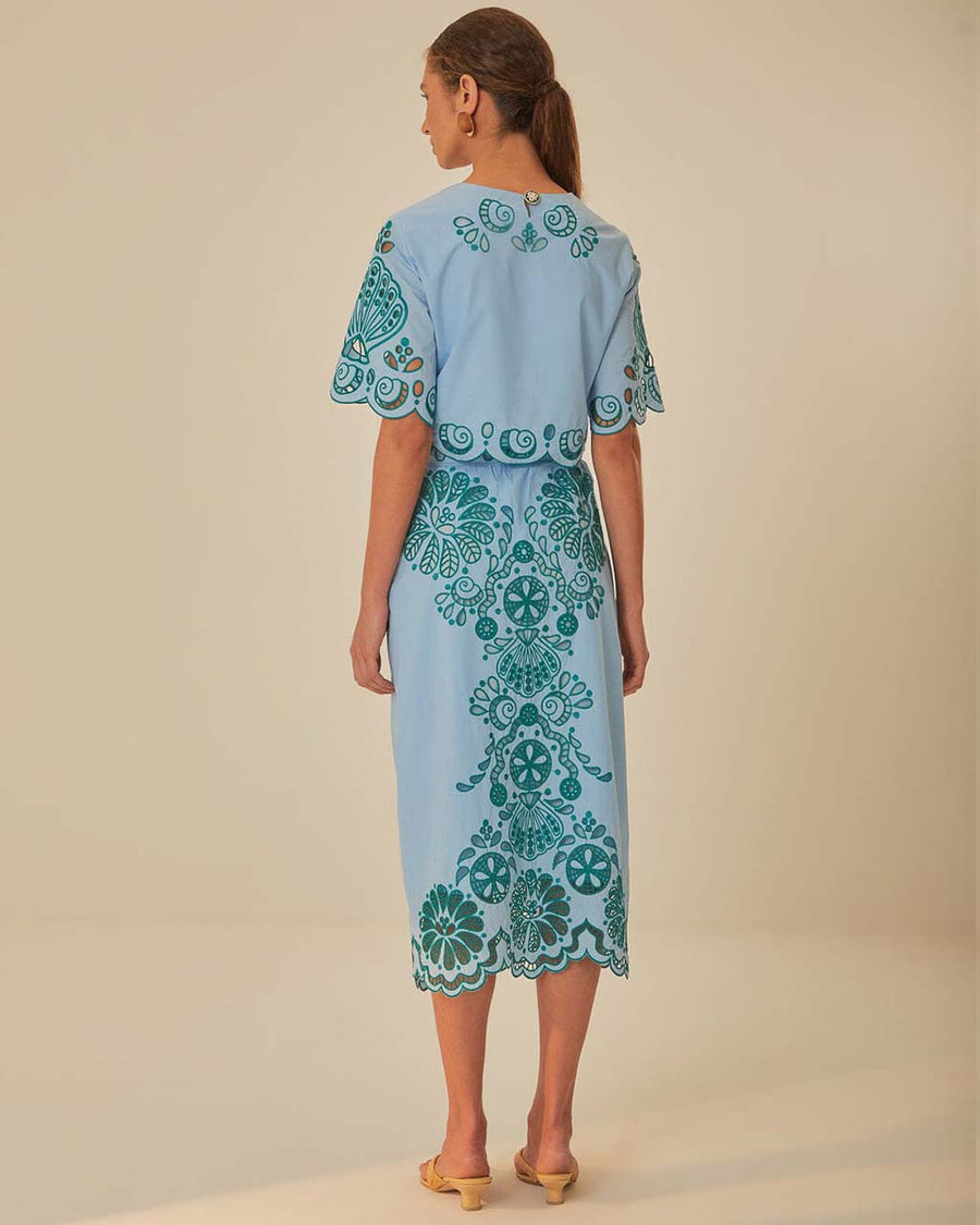 back view of model wearing light blue midi skirt with delicate green cut out pattern and matching top