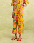 model wearing yellow cropped pants with vibrant flower print, pink piping trim, and pink and yellow flower button