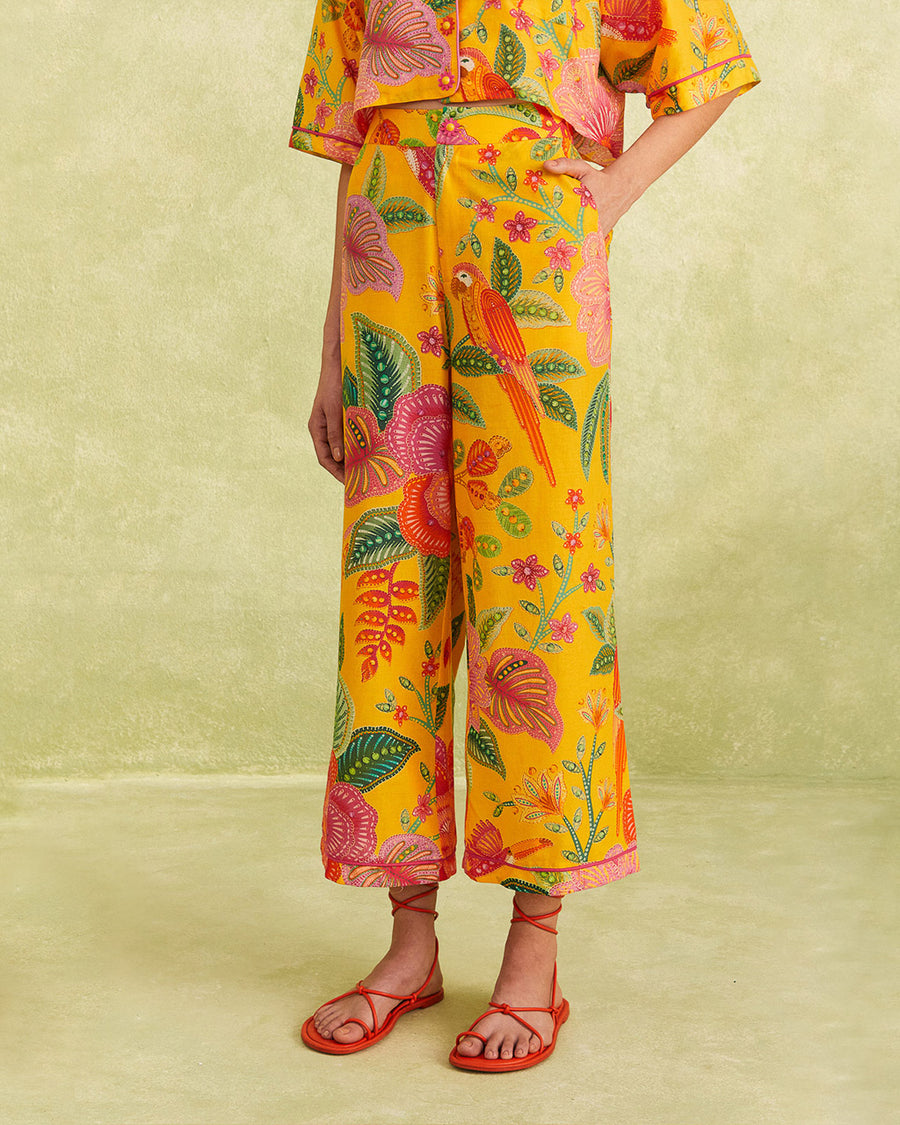 model wearing yellow cropped pants with vibrant flower print, pink piping trim, and pink and yellow flower button