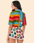 back view of model wearing white crochet shorts with colorful patchwork flowers and rainbow stripe button down