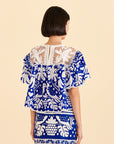 backview of model wearing blue and white jungle top with pom pom detail, ruffle sleeves and crochet neckline
