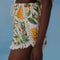 side view of model wearing white shorts with fringe detail, rope tassel drawstring and mixed fruit print