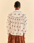 back view of model wearing white button down top with brown piping, tortoise buttons and all over horse print