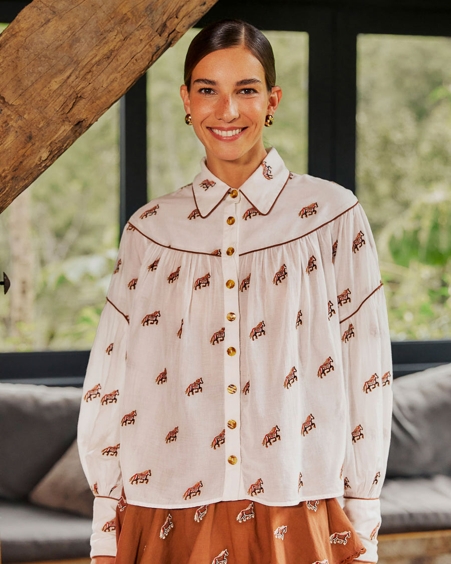 model wearing white button down top with brown piping, tortoise buttons and all over horse print untucked