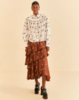 model wearing white button down top with brown piping, tortoise buttons and all over horse print and orange skirt