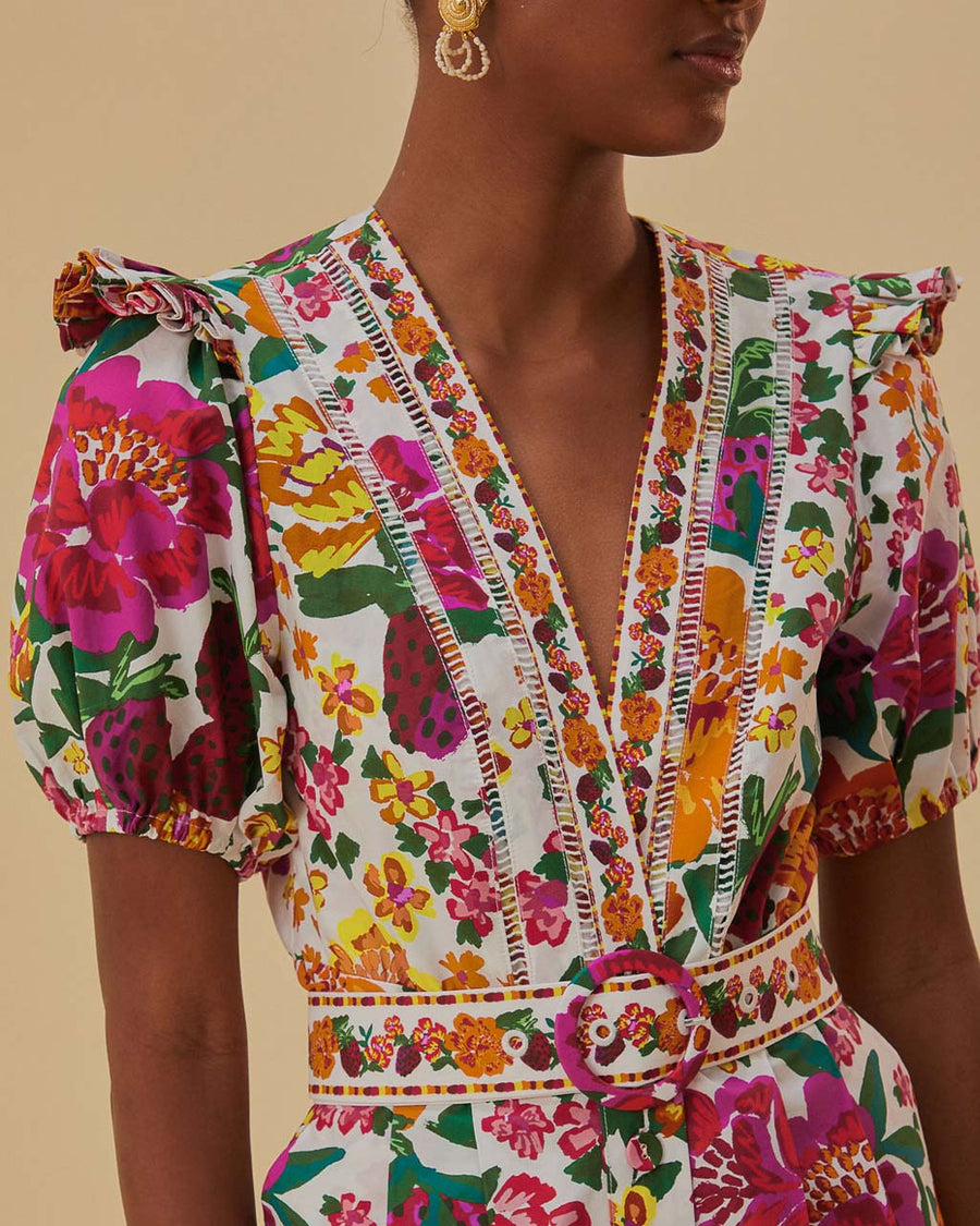 up close of model wearing white romper with colorful floral print, puff sleeves, and belt detail