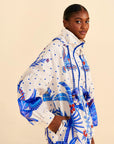 sideview of model wearing white relaxed fit jacket with blue abstract embroidered print and beaded drawstring