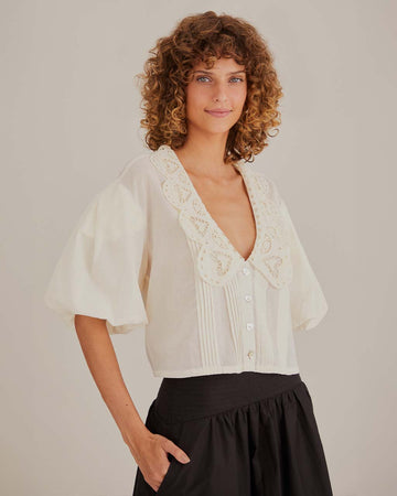 model wearing off white cropped top with puff sleeves, button front, and cut out oversized scalloped collar