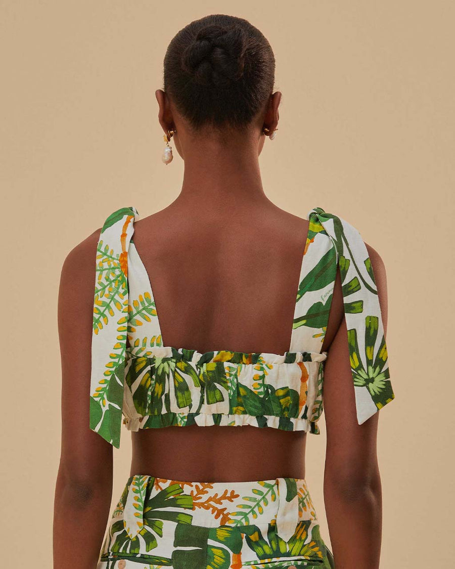 back view of model wearing white cropped tank top with tie straps, ruffle detail and green tropical leaf print