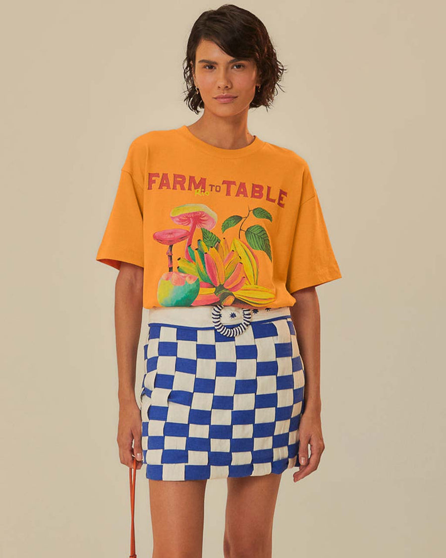 model wearing tucked in orange oversized tee with colorful fruit graphic and 'farm rio to table' typography