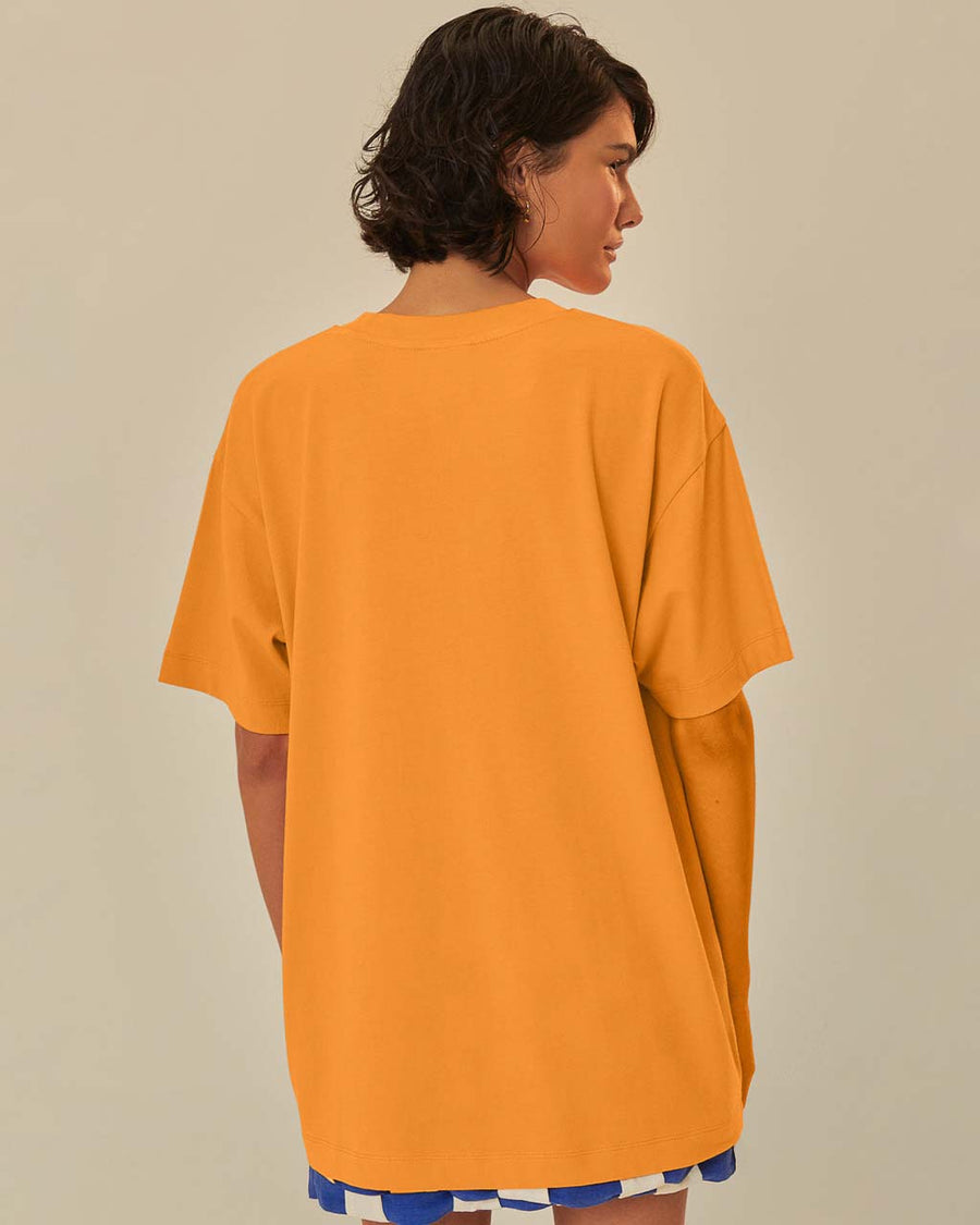 back view of model wearing orange oversized tee with colorful fruit graphic and 'farm rio to table' typography
