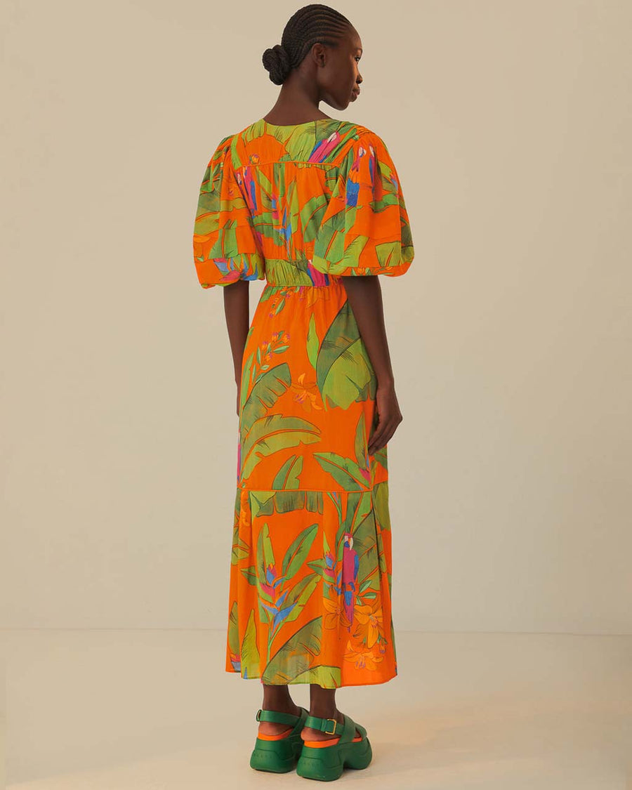 back view of model wearing orange midi dress with puff sleeves, tie waist, deep V neckline and all over leaves and parrot print