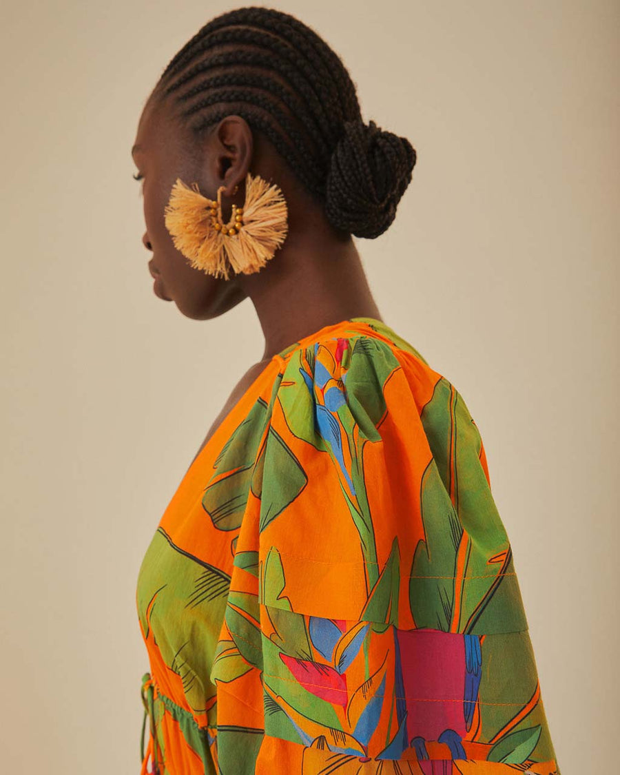 up close of model wearing orange midi dress with puff sleeves, tie waist, deep V neckline and all over leaves and parrot print