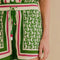 up close of model wearing green shorts with beaded tassel tie, pineapple print and red, white and green stripes down the front