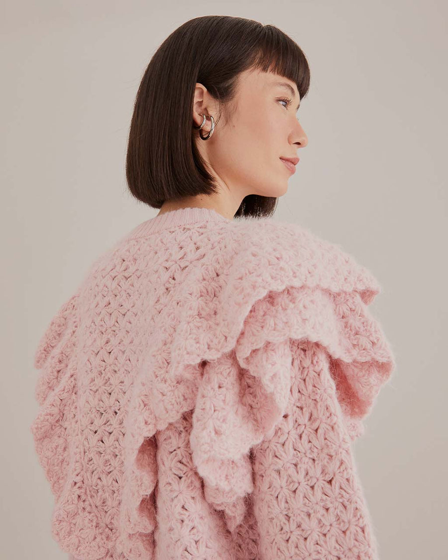 up close of model wearing pink chunky knit cardigan with ruffle shoulders