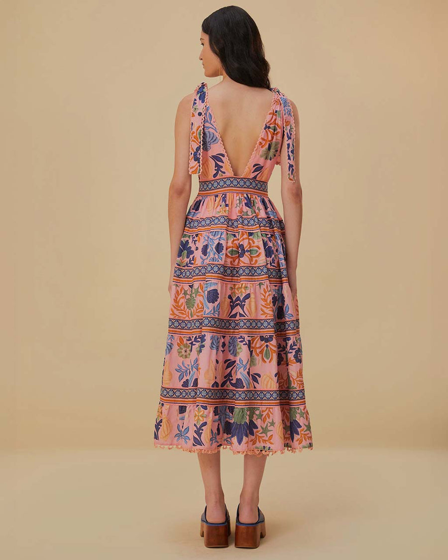 back view of model wearing pink midi dress with deep v neckline, lace hem, tie straps and colorful floral and seashell print