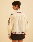 back view of model wearing cream blouse with button front, and all over floral embroidery down the front, sleeves and back