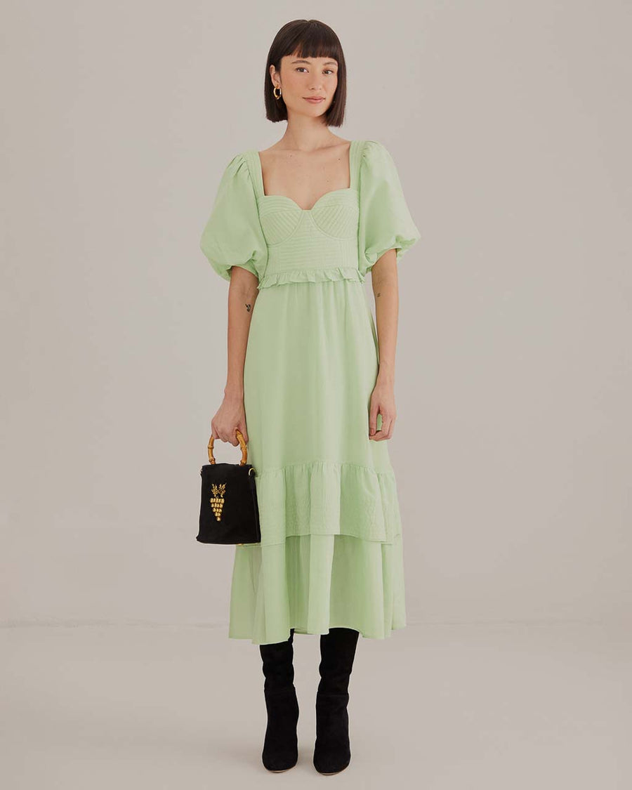 model wearing soft green midi dress with ruffle hem and waist, puff sleeves and stitched corset bodice