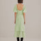 back view of model wearing soft green midi dress with ruffle hem and waist, puff sleeves and stitched corset bodice