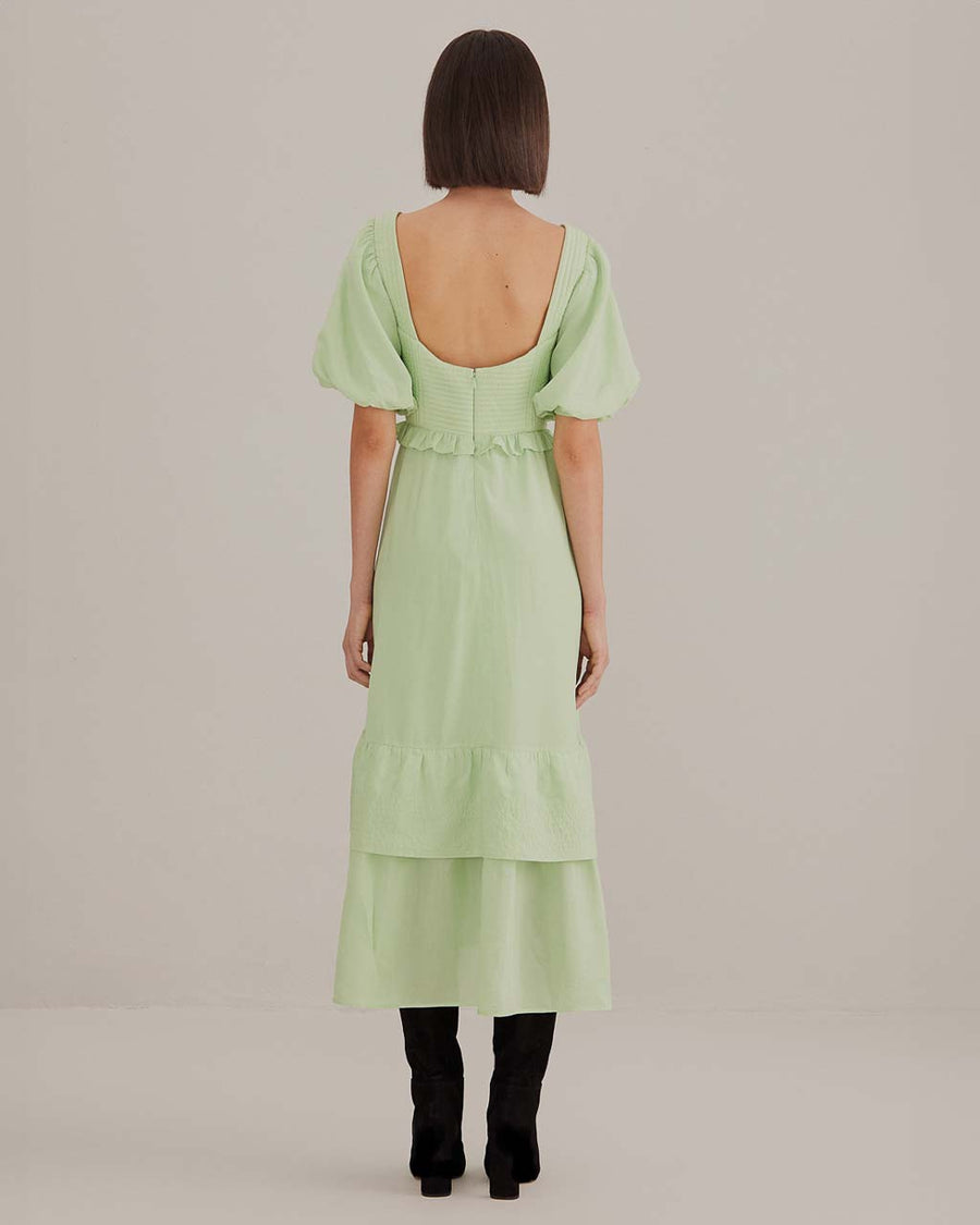 back view of model wearing soft green midi dress with ruffle hem and waist, puff sleeves and stitched corset bodice