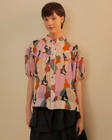 model wearing colorful abstract print with puff short sleeves, button front and ruffle across the bodice