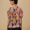 back view of model wearing colorful abstract print with puff short sleeves, button front and ruffle across the bodice