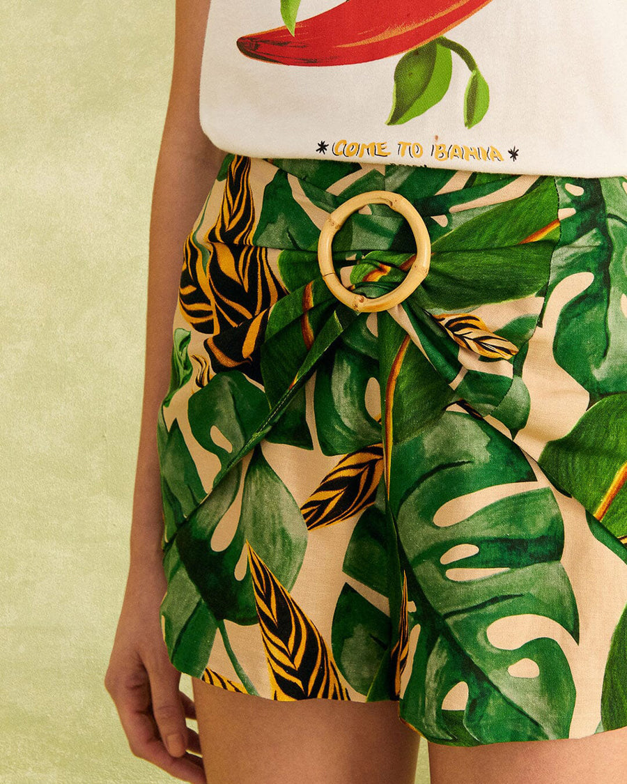 up close of model wearing nude shorts with tropical leaf print, bamboo belt, and white pepper tee
