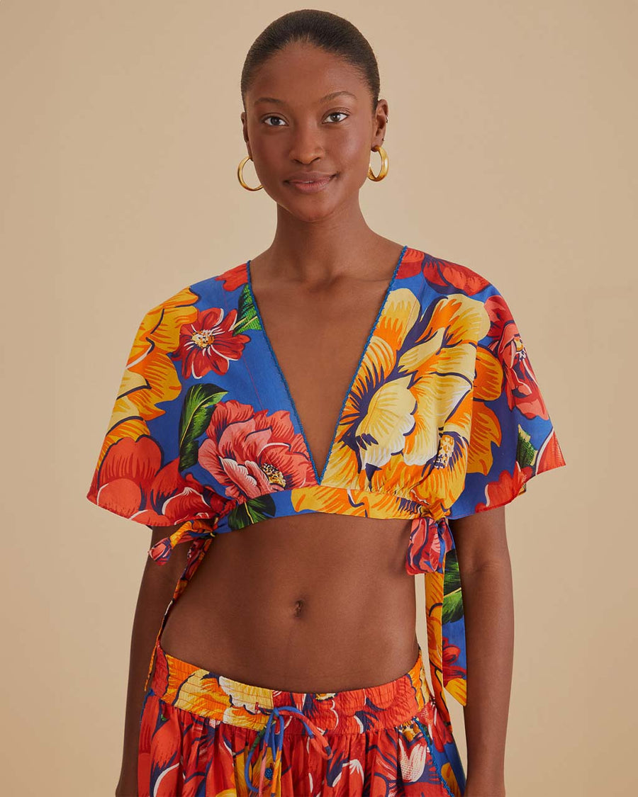 model wearing blue cropped v-neck top with bold yellow, pink and red floral print
