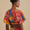 back view of model wearing blue cropped v-neck top with bold yellow, pink and red floral print