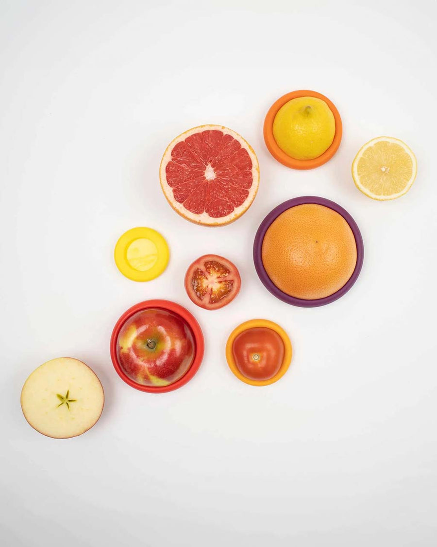 top view of set of 5 various size food huggers in yellow, orange, red and purple shades on various food items