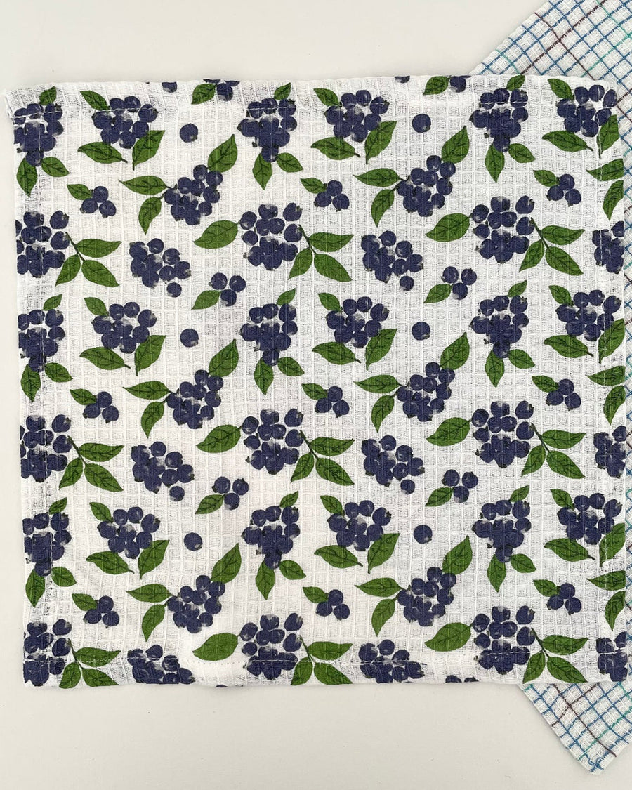 opened set of two woven dishcloths: white with blueberry print and white with plaid in blue, green and burgundy
