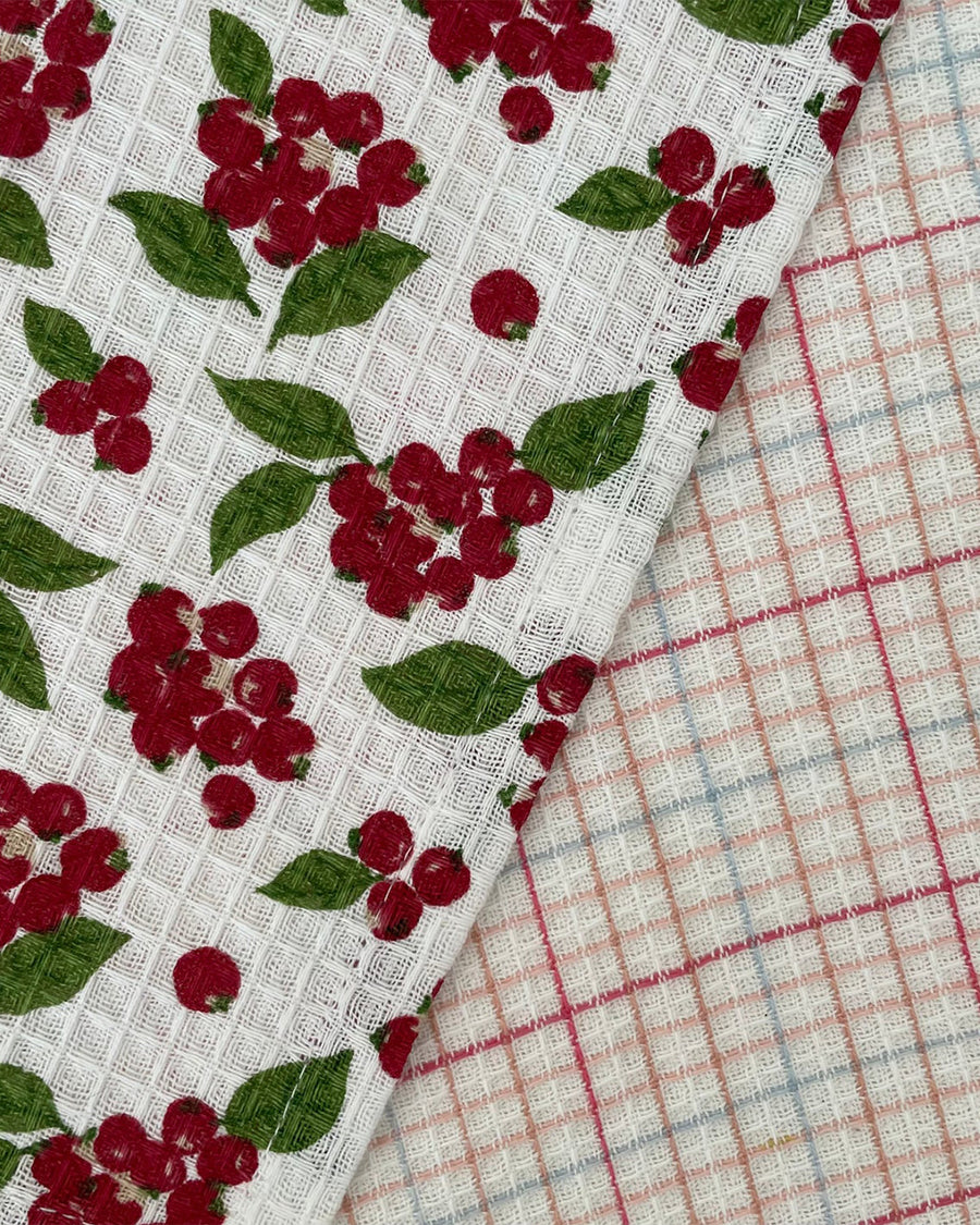 up close of set of two woven dishcloths: white with cranberry and white with plaid in red, pink and blue
