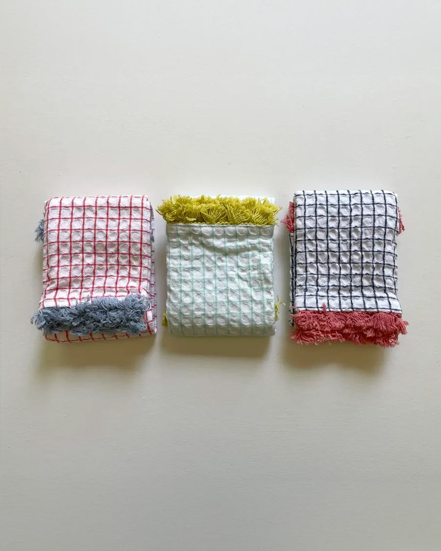 folded set of three plaid dishcloths with fringe: red with blue fringe, mint with yellow fringe, and navy with rose fringe