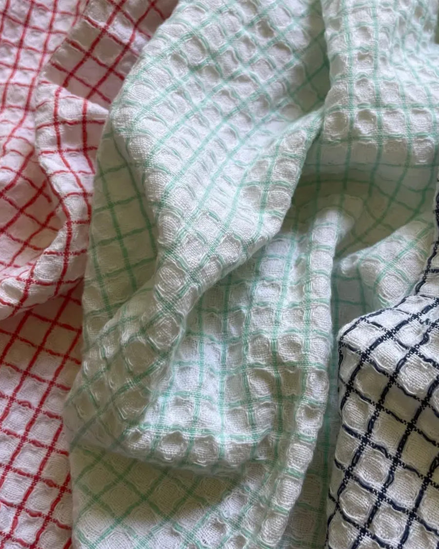 crumpled set of three plaid dishcloths with fringe: red with blue fringe, mint with yellow fringe, and navy with rose fringe