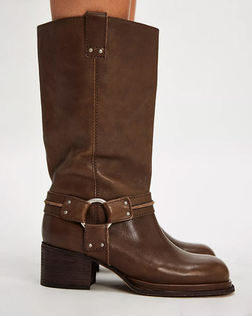 model wearing tall dark brown leather boots with silver buckle and strap detail around the ankle