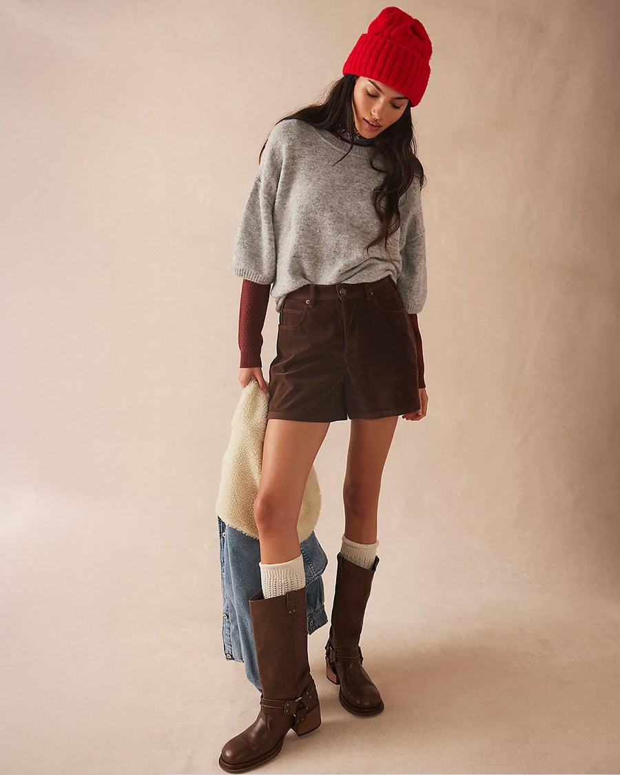 model wearing tall dark brown leather boots with silver buckle and strap detail around the ankle with skirt and sweater