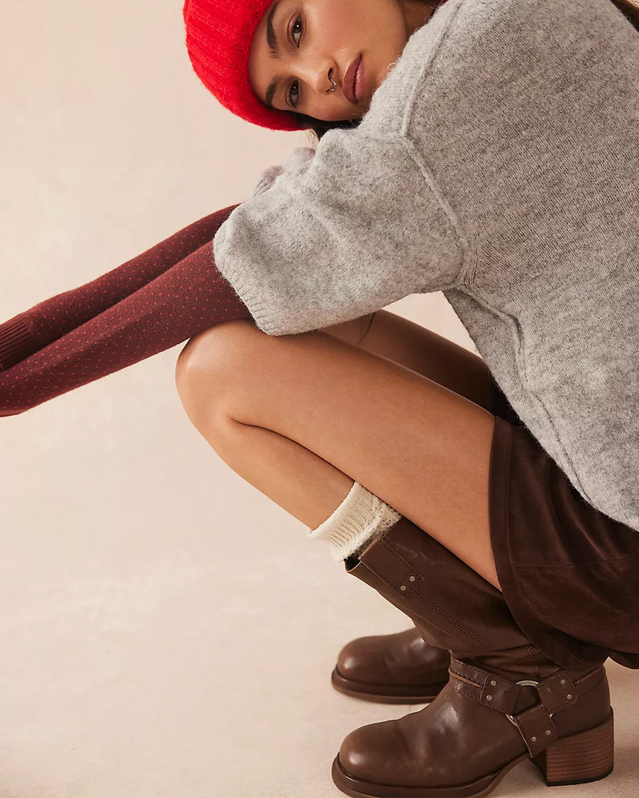 model wearing tall dark brown leather boots with silver buckle and strap detail around the ankle