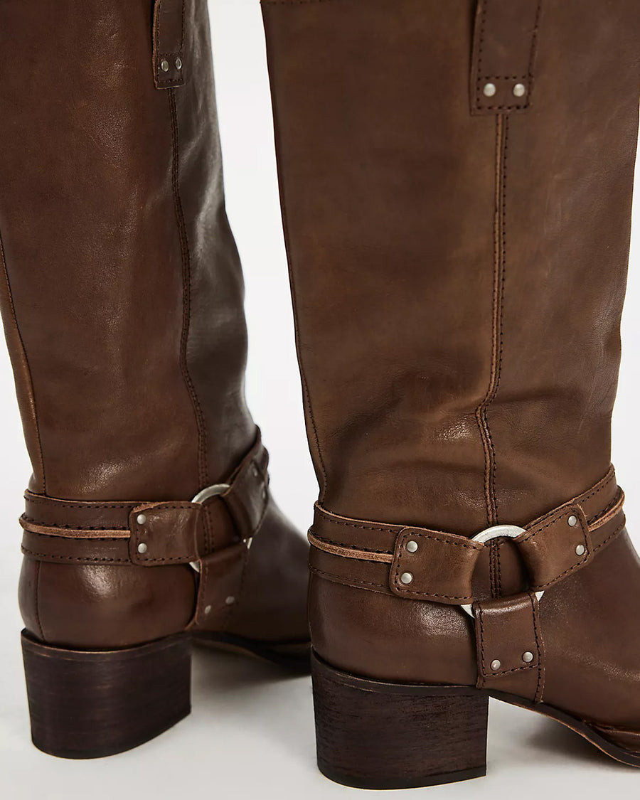 back view of model wearing tall dark brown leather boots with silver buckle and strap detail around the ankle