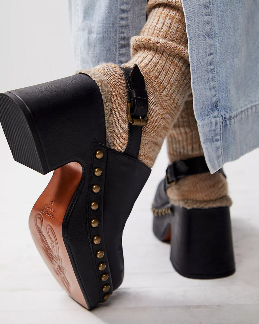 back view of model wearing black leather clogs with gold stud details at the sole