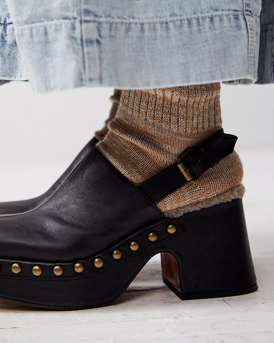 side view of model wearing black leather clogs with gold stud details at the sole