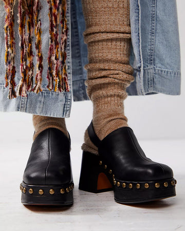 model wearing black leather clogs with gold stud details at the sole