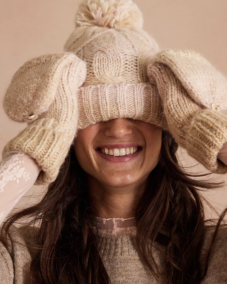 model wearing thick knit ivory winter hat with pom and fingerless gloves/mittens