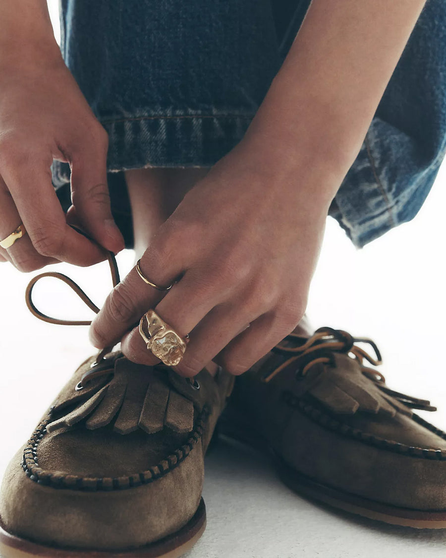 model wearing taupe suede slip on boat shoe with tie top and fringe detail