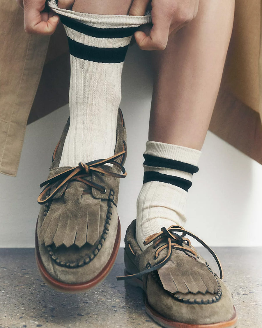 model wearing taupe suede slip on boat shoe with tie top and fringe detail and white crew socks