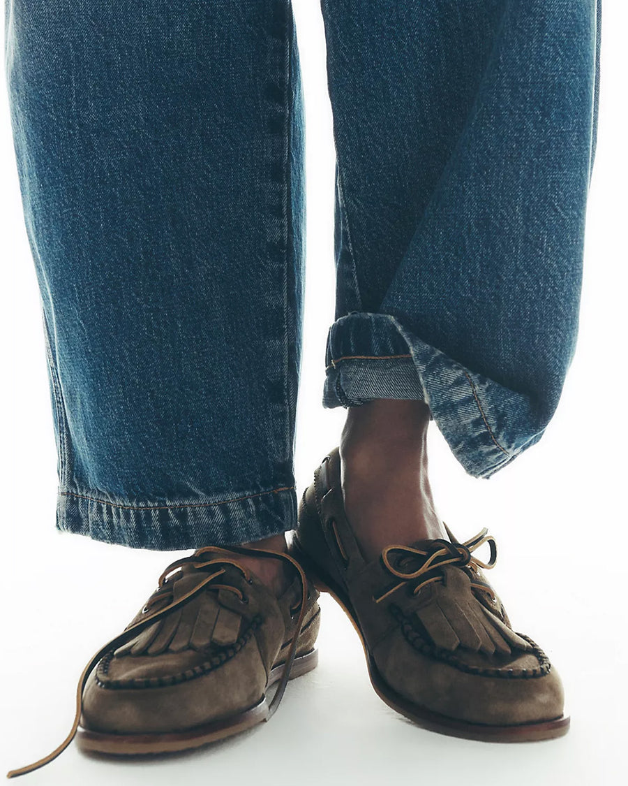 model wearing taupe suede slip on boat shoe with tie top and fringe detail