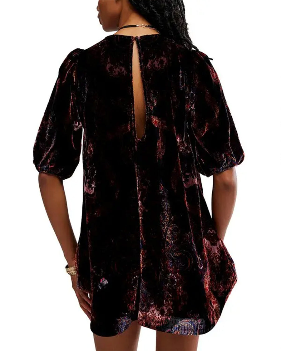 back view of model wearing black velvet tunic with red and burgundy floral print, short sleeve puff sleeves and open keyhole back