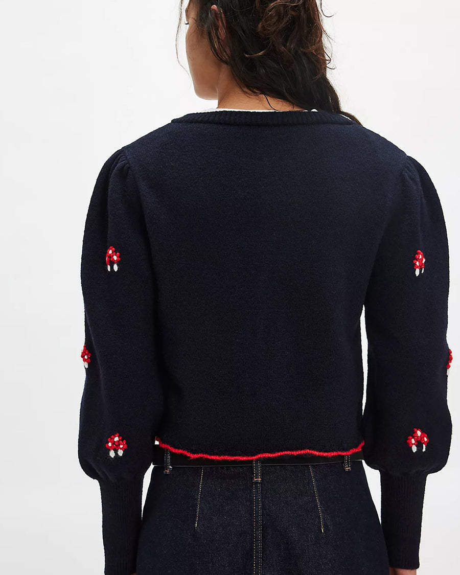 back view of model wearing black cropped cardigan with red folk floral print on the front and sleeves