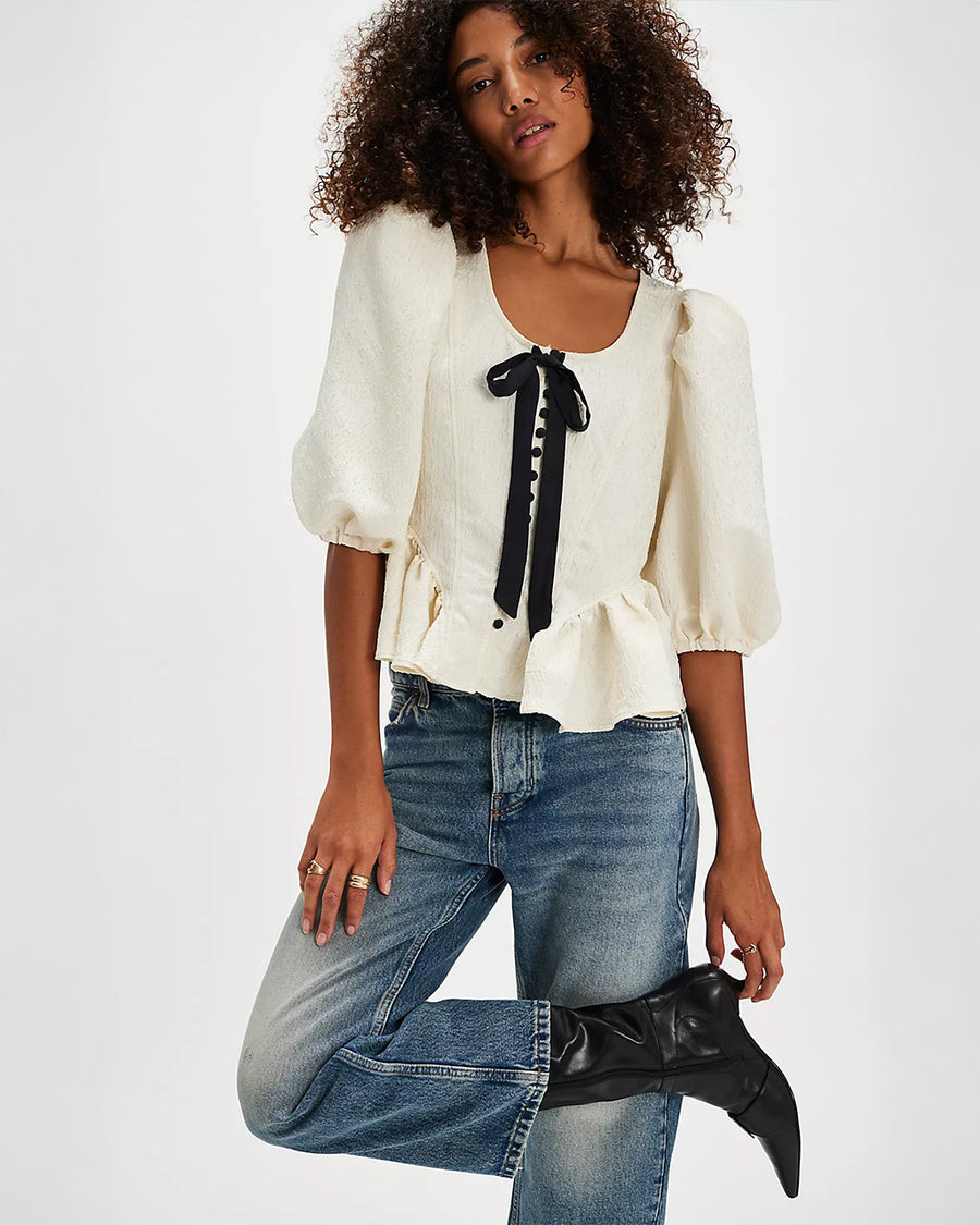 model wearing jacquard blouse with puff sleeves, slight peplum hem, and black bow and buttons on the bust