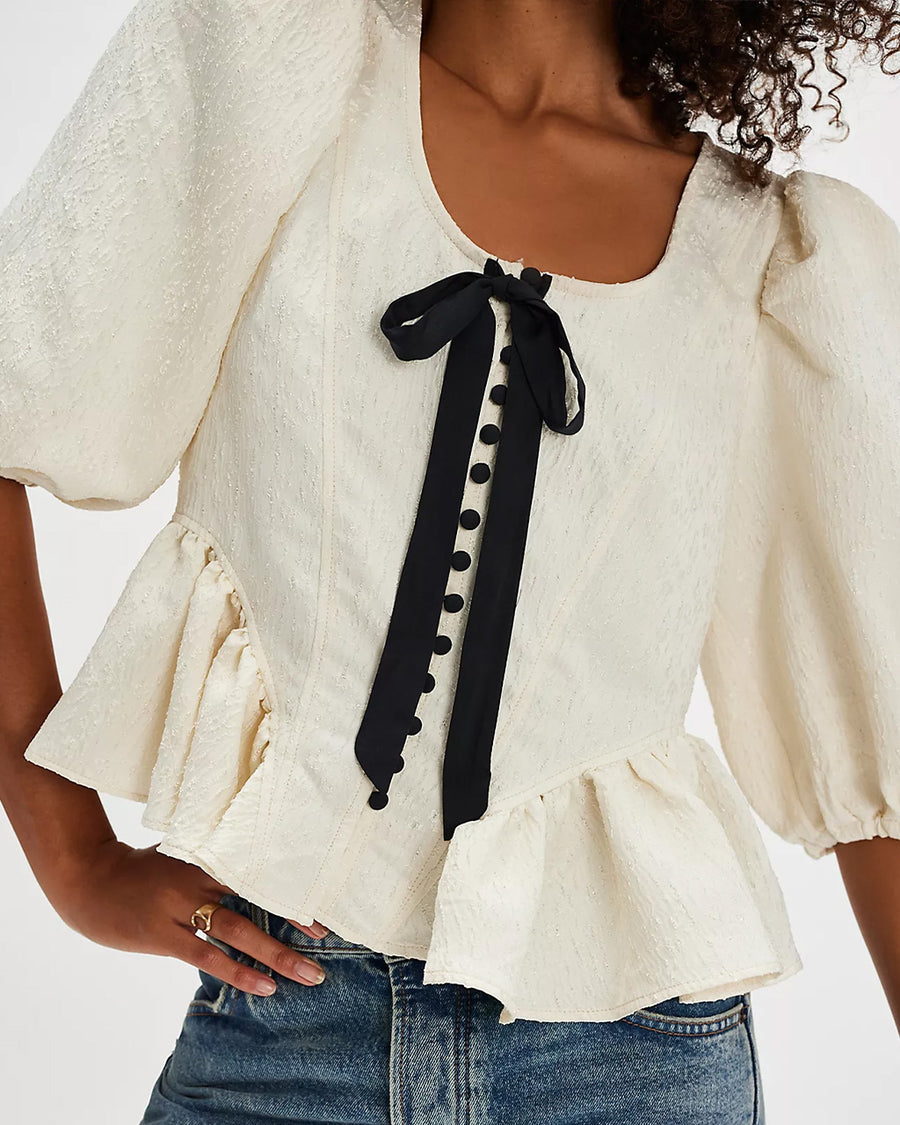 model wearing jacquard blouse with puff sleeves, slight peplum hem, and black bow and buttons on the bust