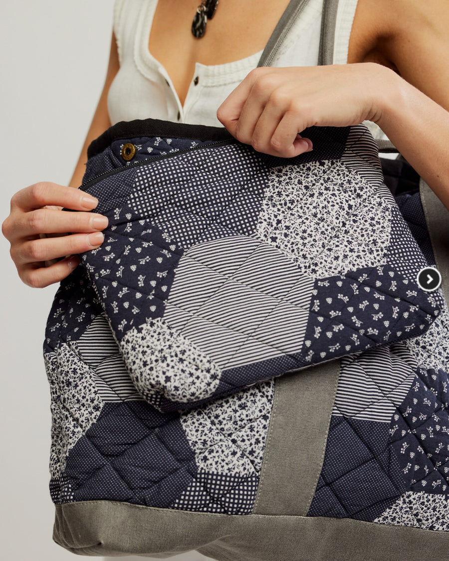 model holding blue, black and grey quilted patchwork bag with matching zip pouch